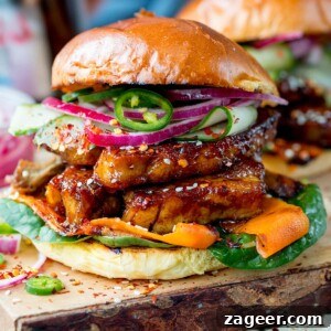 Sticky Glazed Pork Burger with Quick Pickled Veggies 7 Square side-on image of toasted brioche roll filled with sticky pork belly strips and pickled carrot, red onion and cucumber strips. Topped with jalapeno slices. Served on a wooden board.