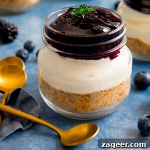 Mini No-Bake Berry Cheesecakes: Individual Dessert Cups 18 Individual berry cheesecake in a mason jar on a blue background next to a gold teaspoon