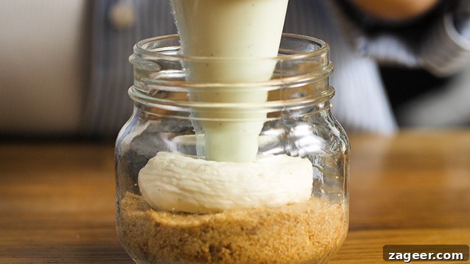Mini No-Bake Berry Cheesecakes: Individual Dessert Cups 6 Cheesecake mixture being piped into a mason jar on top of a crushed biscuit base.