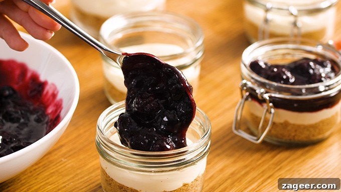 Mini No-Bake Berry Cheesecakes: Individual Dessert Cups 9 Spooning berry mixture on top of mason jar cheesecakes