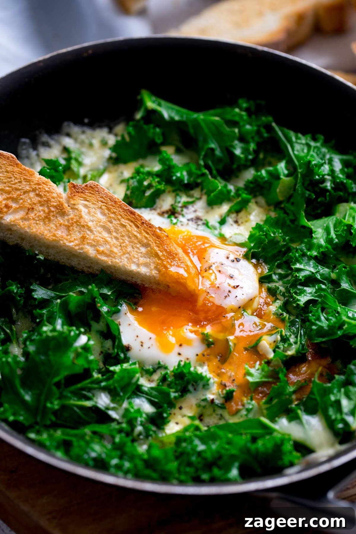 Creamy Scrambled Eggs with Sautéed Kale Breakfast Bowl 2 A toast soldier being dipped into the runny egg yolk in a pan of kale and fried egg.