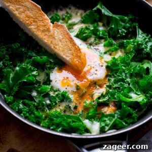 Creamy Scrambled Eggs with Sautéed Kale Breakfast Bowl 6 A toast soldier being dipped into a runny egg yolk in a pan of egg and cheesy kale