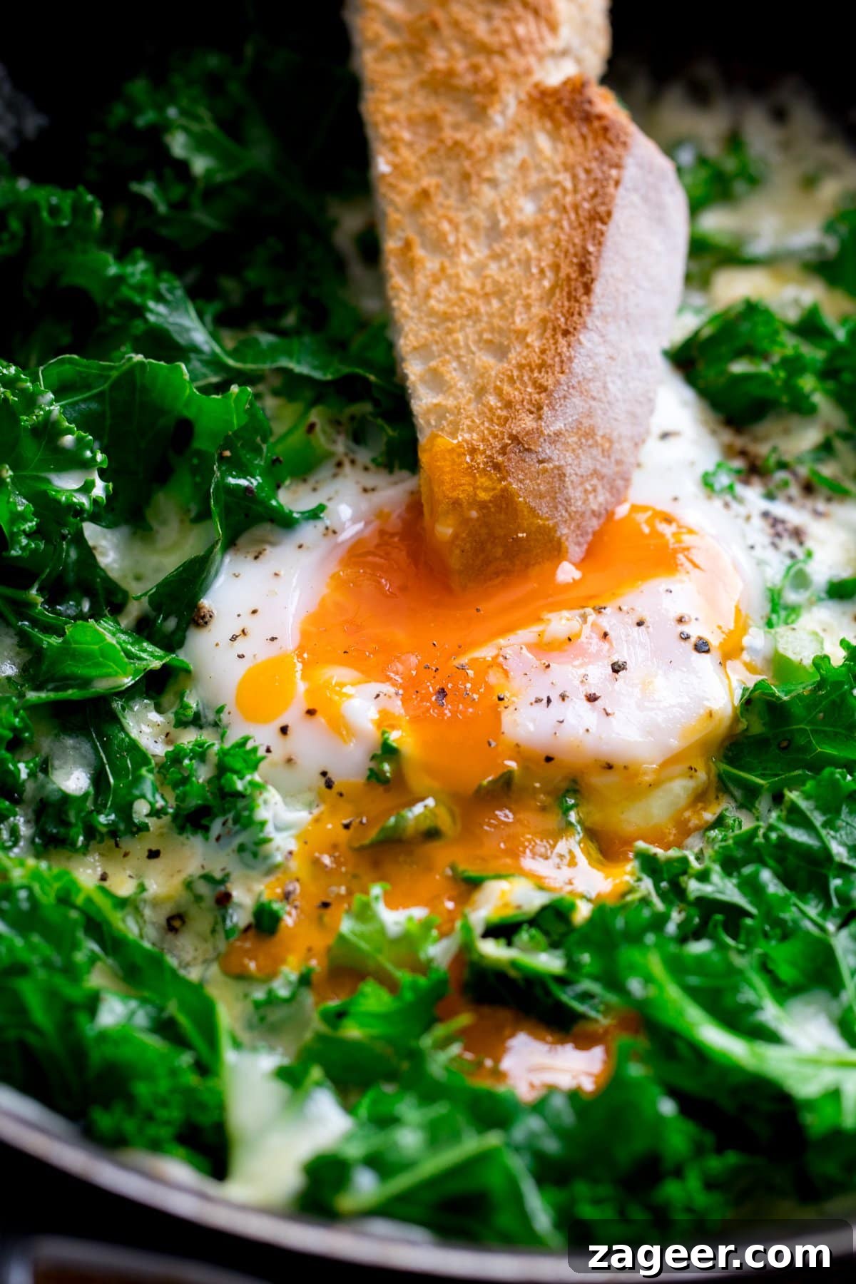 Creamy Scrambled Eggs with Sautéed Kale Breakfast Bowl 5 Close up of a toast soldier being dipped into a runny egg in a pan of egg and cheesy kale