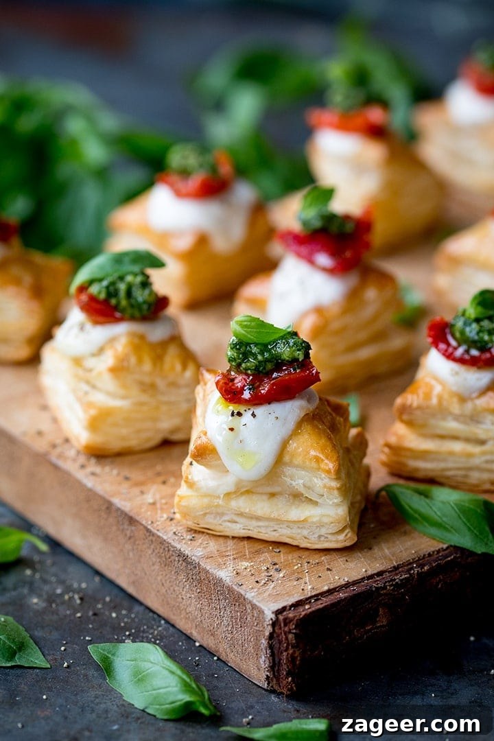 Caprese Puff Pastry Bites: Tomato, Basil & Mozzarella Appetizers 2 Close up of puff pastry caprese bites - with mozzarella, pesto and sundried tomato - on a serving board