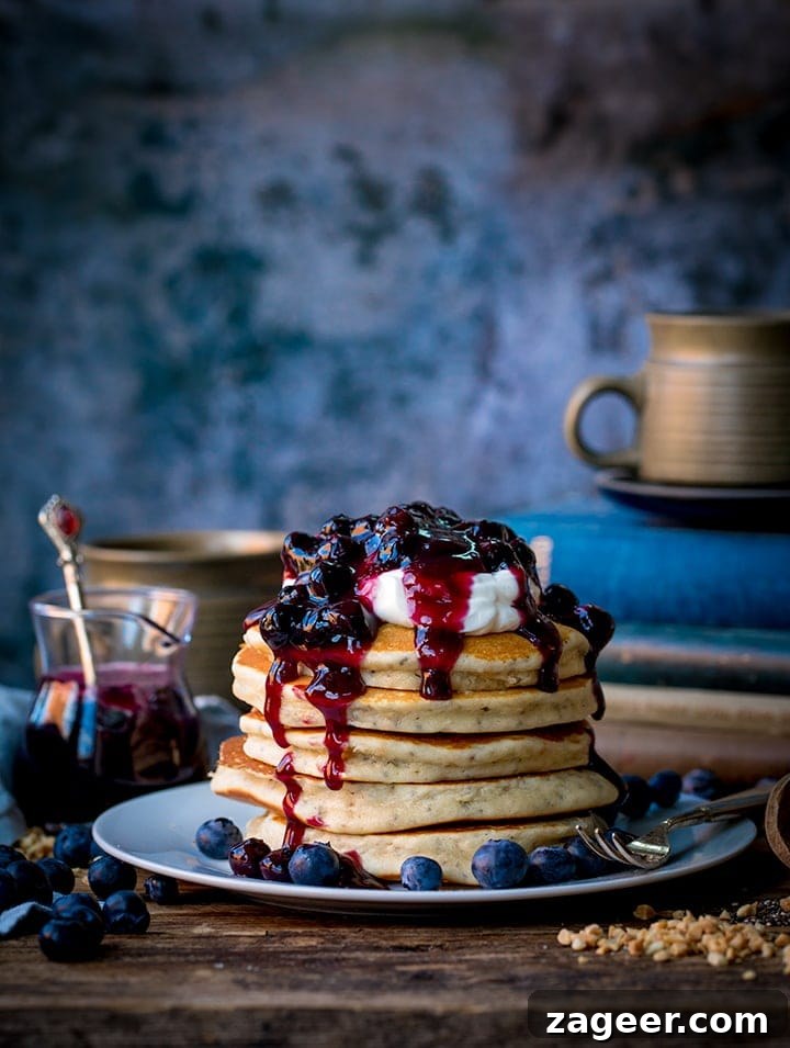 Gluten-Free Hazelnut Chia Pancakes with Blueberry Compote 2 Stack of chia hazelnut pancakes on a plate with greek yogurt and blueberry compote dripping down