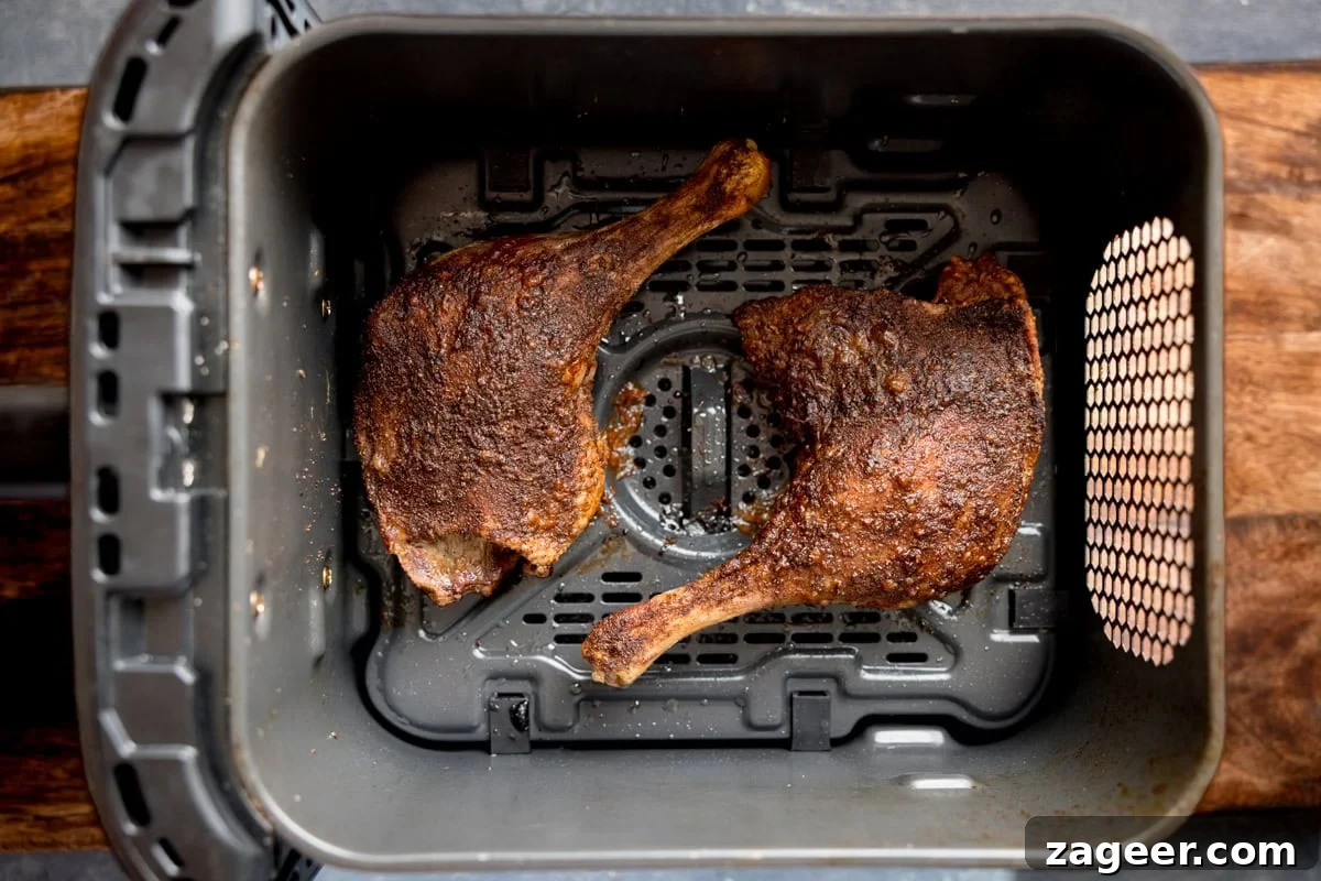 Crispy Homemade Roast Duck Recipe for Perfectly Crunchy Skin 11 Two cooked crispy duck legs with seasoned skin sit inside the basket of an air fryer on a wooden worktop.