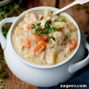 Creamy Chicken Pot Pie Soup Recipe — Comfort in a Bowl 6 A white bowl filled with creamy chicken pot pie soup containing pieces of chicken, carrots, celery and potatoes, topped with fresh thyme.