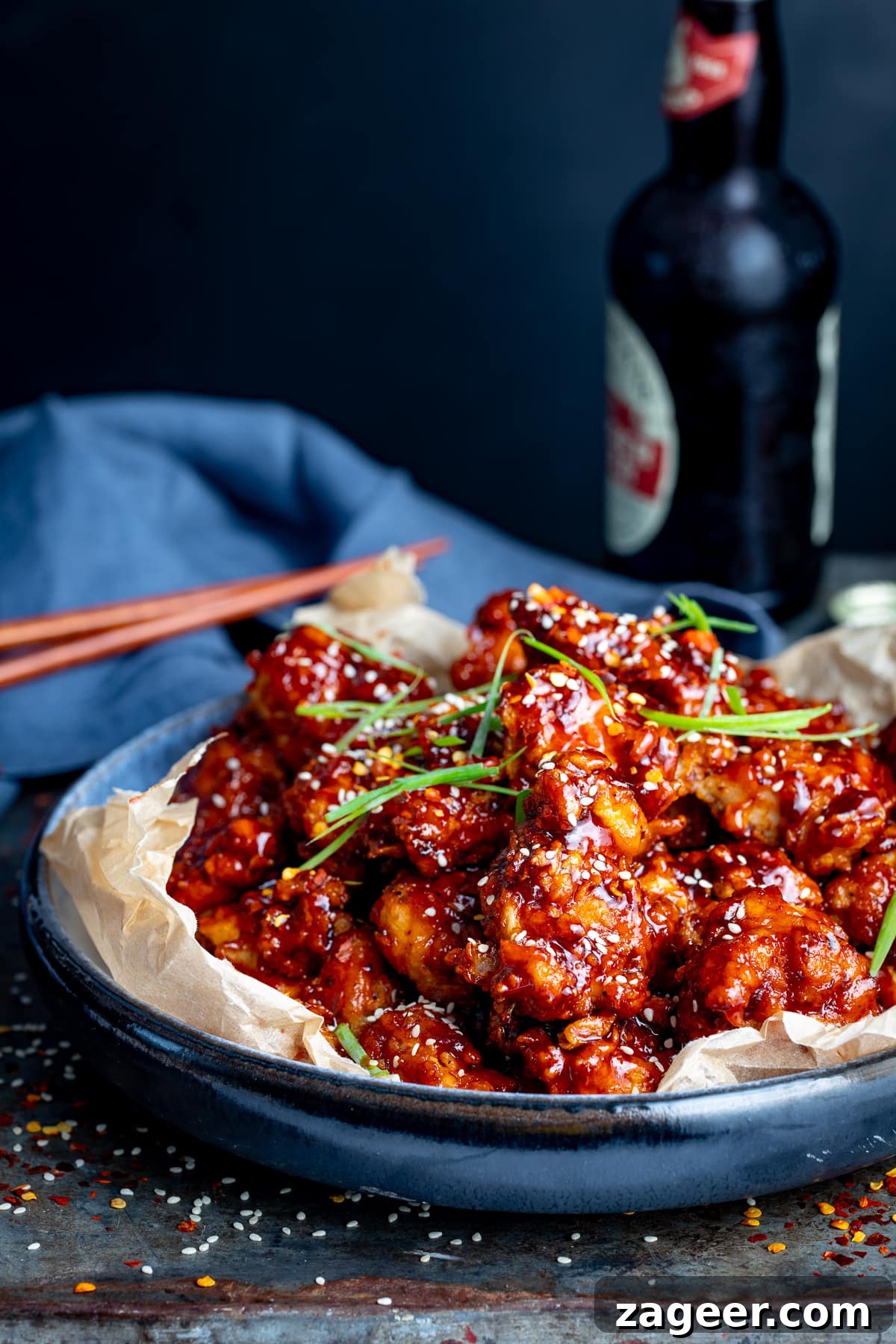 Korean fried chicken in a blue bowl against a dark background. Dark bottle and chopsticks in the background.