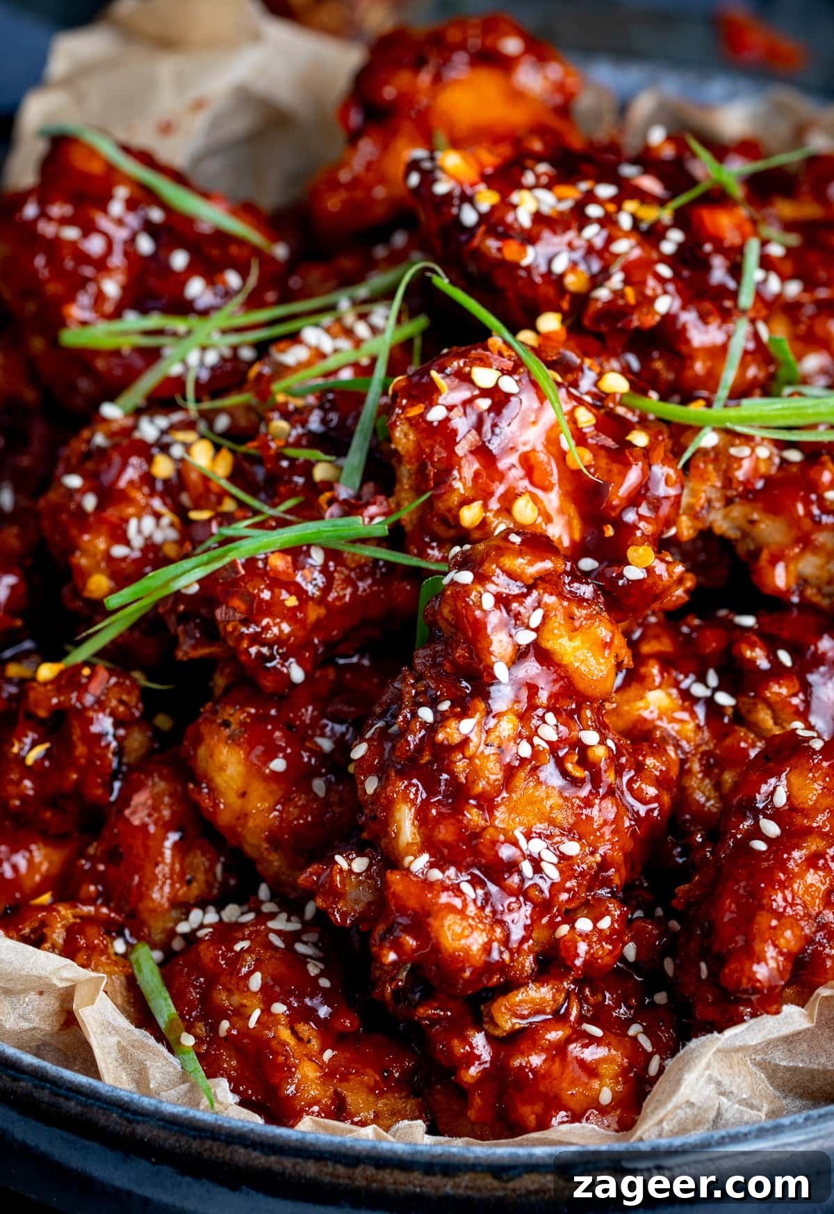 Close up shot of a bowl of Korean fried chicken topped with sesame seeds and strips of spring onion.