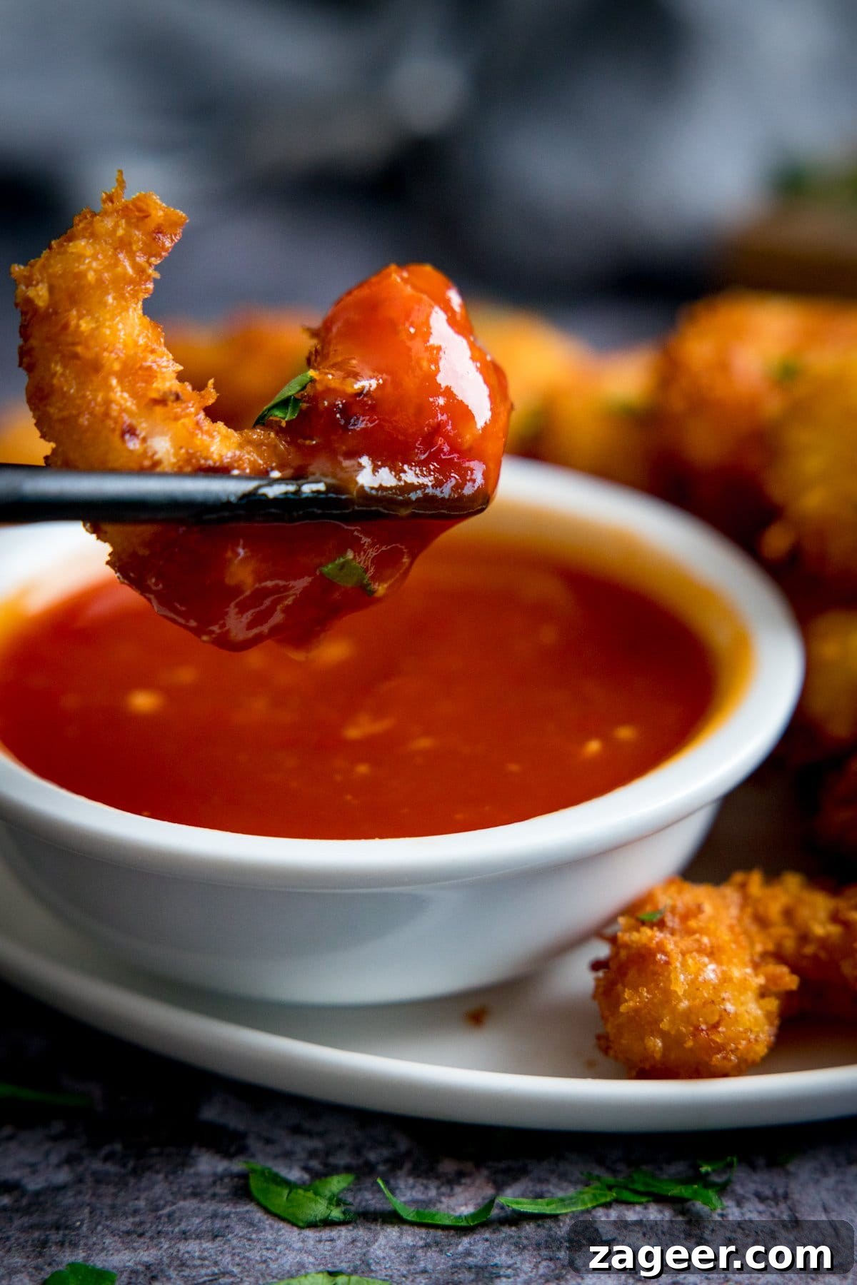 Crispy Coconut Shrimp Recipe with Mango Dipping Sauce 5 Coconut shrimp being dipped into a dish of sweet and sour sauce using chopsticks
