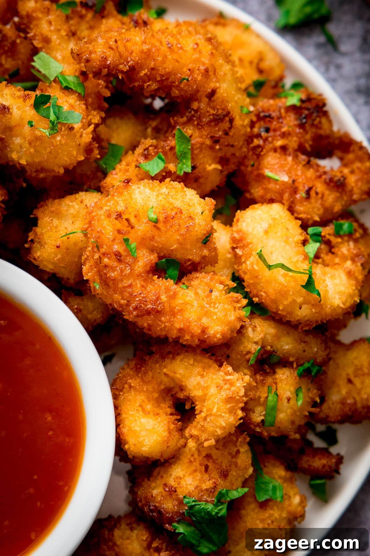 Crispy Coconut Shrimp Recipe with Mango Dipping Sauce 6 Close up of coconut shrimp on a plate next to a dish of sweet and sour sauce.