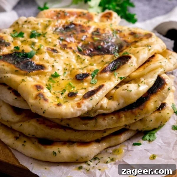 Authentic Chicken Tikka Masala Recipe for Tender, Creamy Curry 11 Pile of garlic naan breads on a piece of parchment on top of a wooden board.