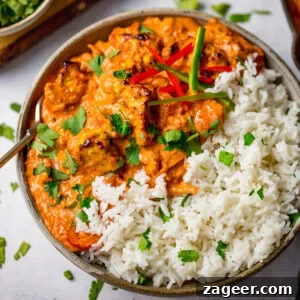 A bowl of chicken tikka masala with white rice, garnished with chopped coriander and sliced chilli peppers.
