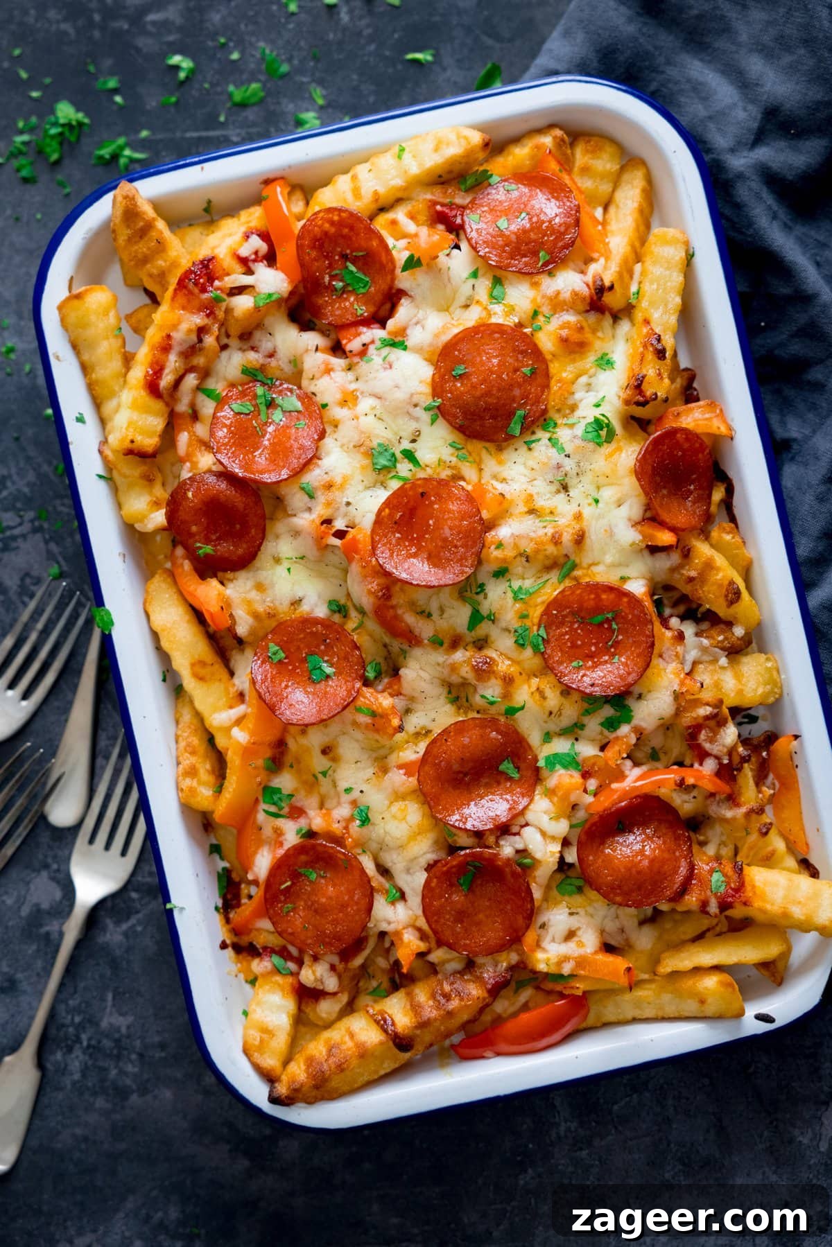 Crispy Pizza Fries Recipe: Loaded Seasoned Potato Bites 2 Overhead shot of pizza fries on a white tray on a dark background. Forks and a blue napkin are around the tray.