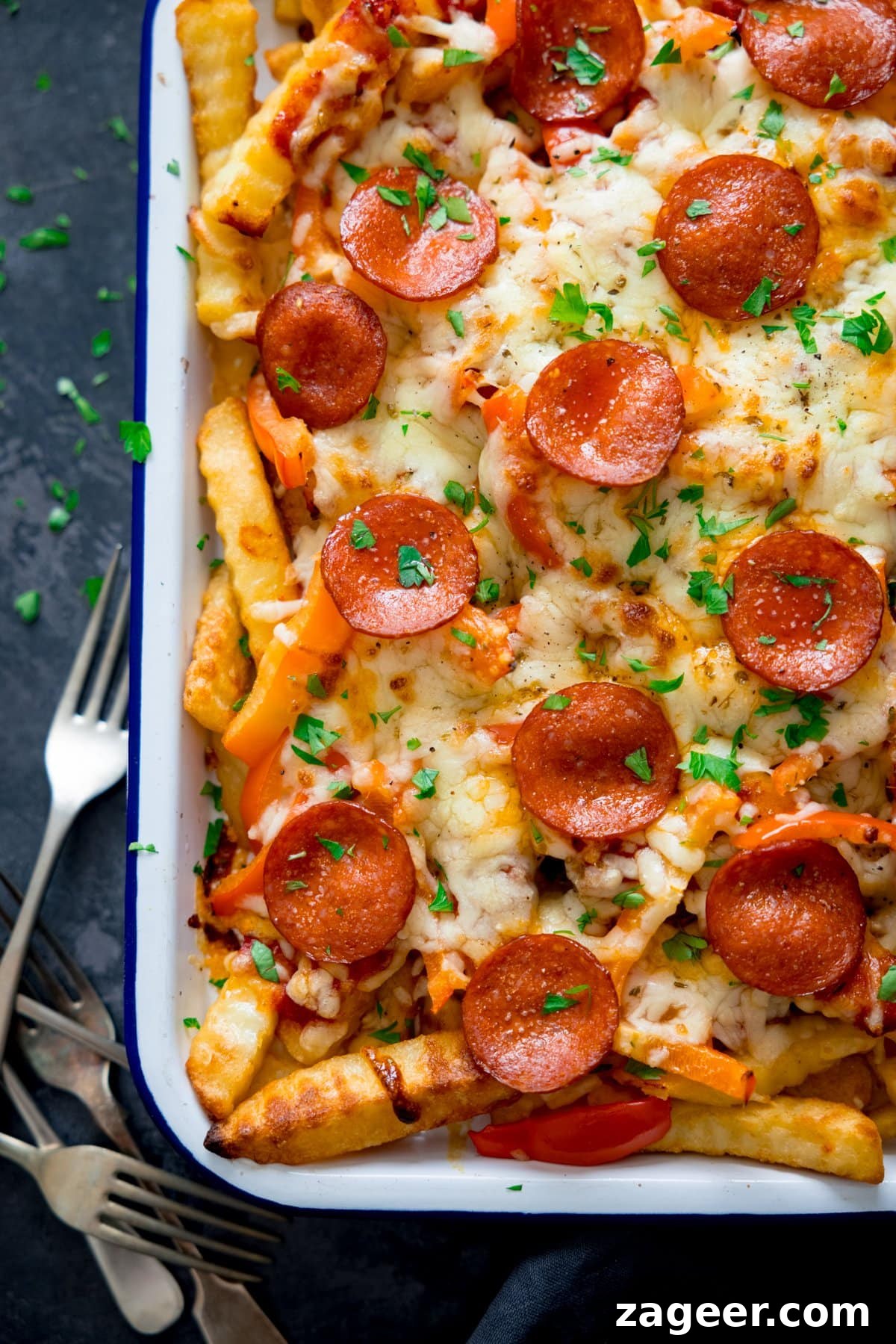 Crispy Pizza Fries Recipe: Loaded Seasoned Potato Bites 5 Overhead shot of pizza fries on a white tray on a dark background next to a small pile of forks