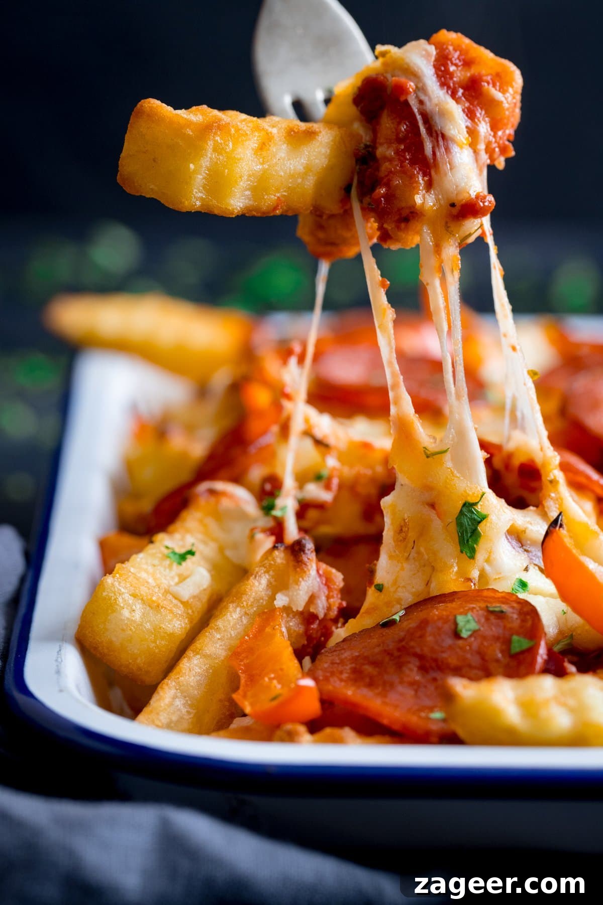 Crispy Pizza Fries Recipe: Loaded Seasoned Potato Bites 6 Forkful of pizza fries being taken from a tray with a fork. The cheese is stretching as the forkful is being lifted.