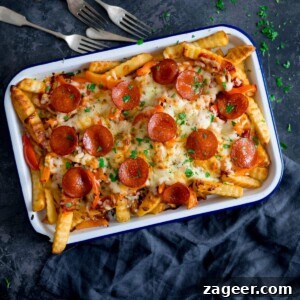 Crispy Pizza Fries Recipe: Loaded Seasoned Potato Bites 7 Square image of pizza fries on a white baking tray on a dark blue background with a blue napkin and forks around the tray.