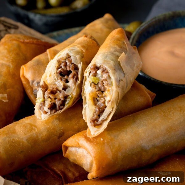 Mini Chicken and Bean Burritos with Zesty Salsa Recipe 11 A square shot of Cheeseburger Spring Rolls. There are 6 whole spring rolls stacked horizontally next to each other, and on top of the stack (in the middle of the image) there is another spring roll that has been cut in half and the two halves are arranged next to each other so you can see the filling. This is set on a wooden board. In the right of the background, you can see a dark blue dish filled with burger sauce. And in the top left of the background, you can slightly see another blue dish with pickled gherkins in it. This is all set on a navy blue background.