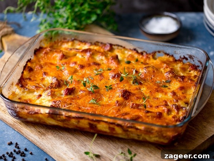 Creamy Scalloped Potatoes with Ham and Cheese Bake 12 wide image of Scalloped potatoes with ham in a glass dish sat on a wooden board.