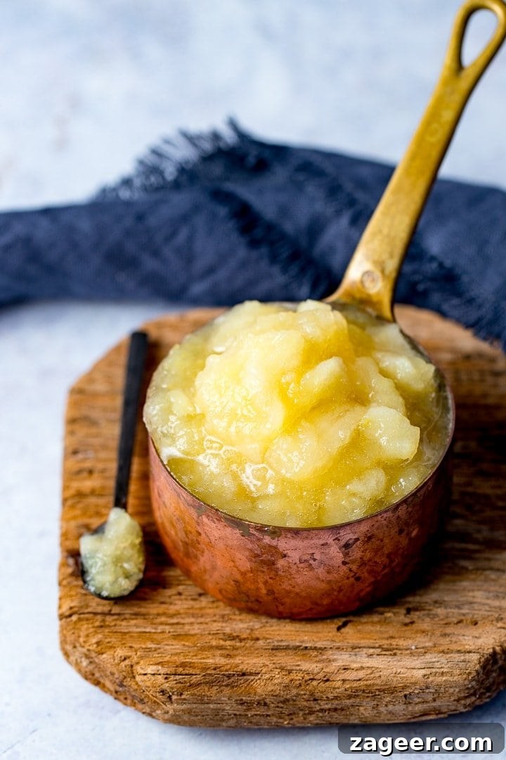 Homemade Applesauce from Scratch: Simple, Flavorful Recipe 2 Apple sauce in a copper pan on a wooden board with a spoonful taken out