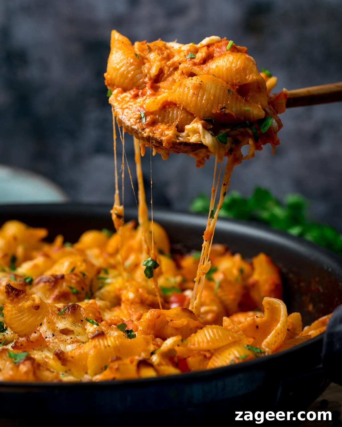 Cheesy Tomato and Tuna Pasta Bake Recipe 2 A pan of Creamy Tomato Tuna Pasta Bake with melted cheese, served in tomato sauce, is being served with a wooden spoon. The cheese is stretching as the portion is being lifted from the pan.