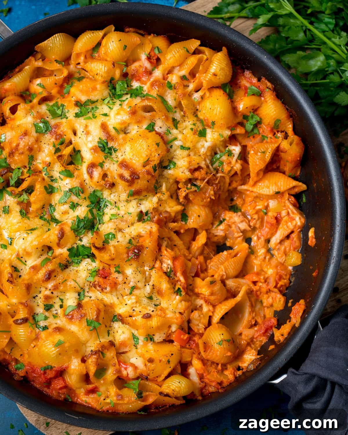 Cheesy Tomato and Tuna Pasta Bake Recipe 6 Tuna pasta bake with pasta shells in a frying pan, topped with melted cheese and chopped parsley, with a portion served out to reveal creamy tomato sauce.