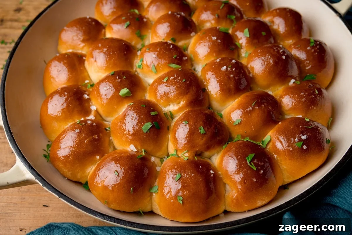 Cheesy Tomato and Tuna Pasta Bake Recipe 7 A baking dish filled with golden, glossy dough balls, each topped with a sprinkle of salt and garnished with chopped parsley. The rolls are closely packed, creating a visually appealing pattern. A blue cloth is partially visible underneath the dish for an enticing touch.