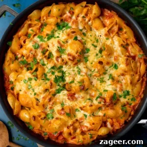 Cheesy Tomato and Tuna Pasta Bake Recipe 8 Overhead image of a creamy tuna tomato pasta bake topped with melted cheese and chopped parsley. The dish is on a blue surface.
