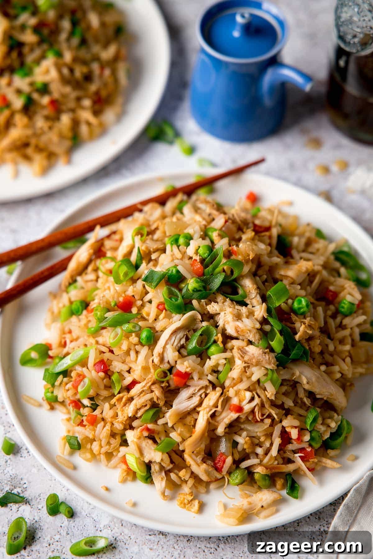 Ultimate Chicken Fried Rice Recipe for Flavorful Weeknight Meals 2 Chicken Fried Rice on a white plate with chopsticks. The plate is on a light background. There is a further plate of chicken fried rice in the background, along with a blue soy sauce pot.