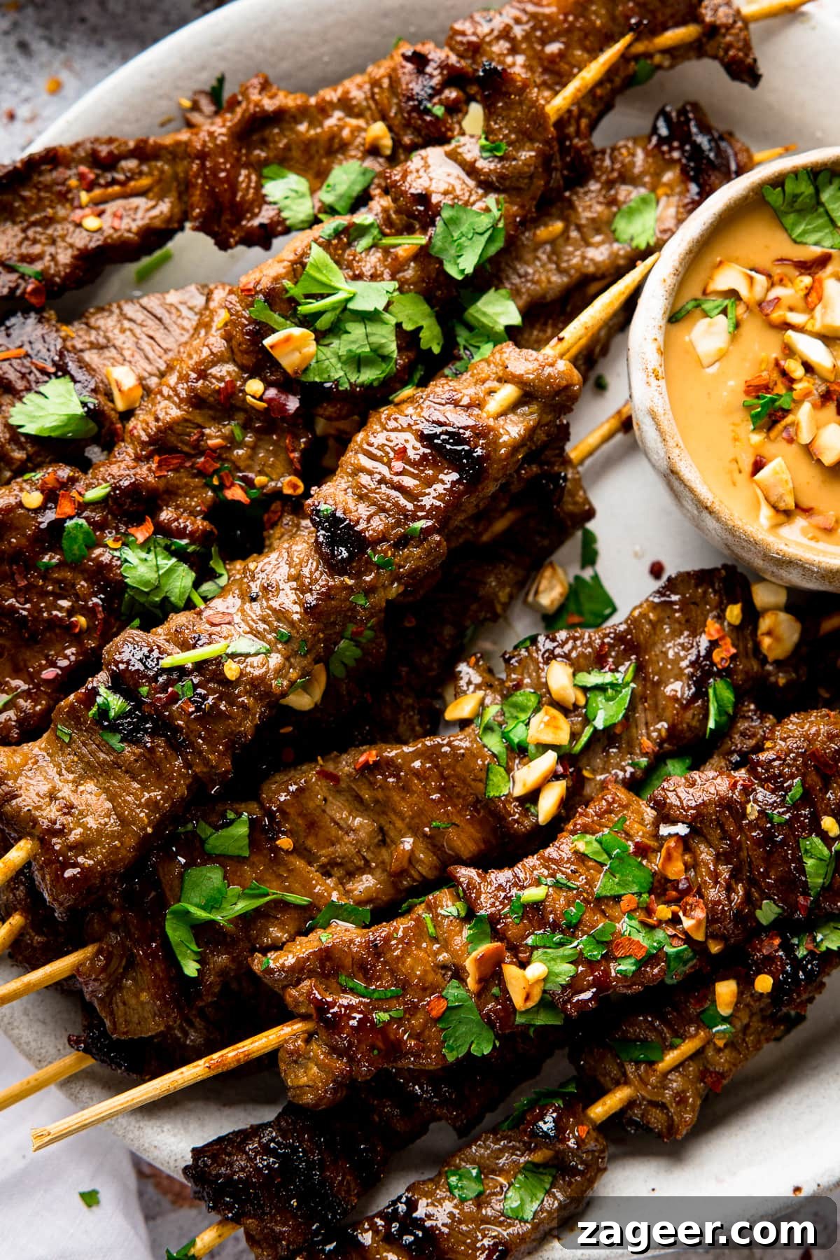 Grilled Beef Satay Recipe: Tender Skewers with Peanut Sauce 2 Close up of beef satay skewers on a plate, topped with coriander and peanuts