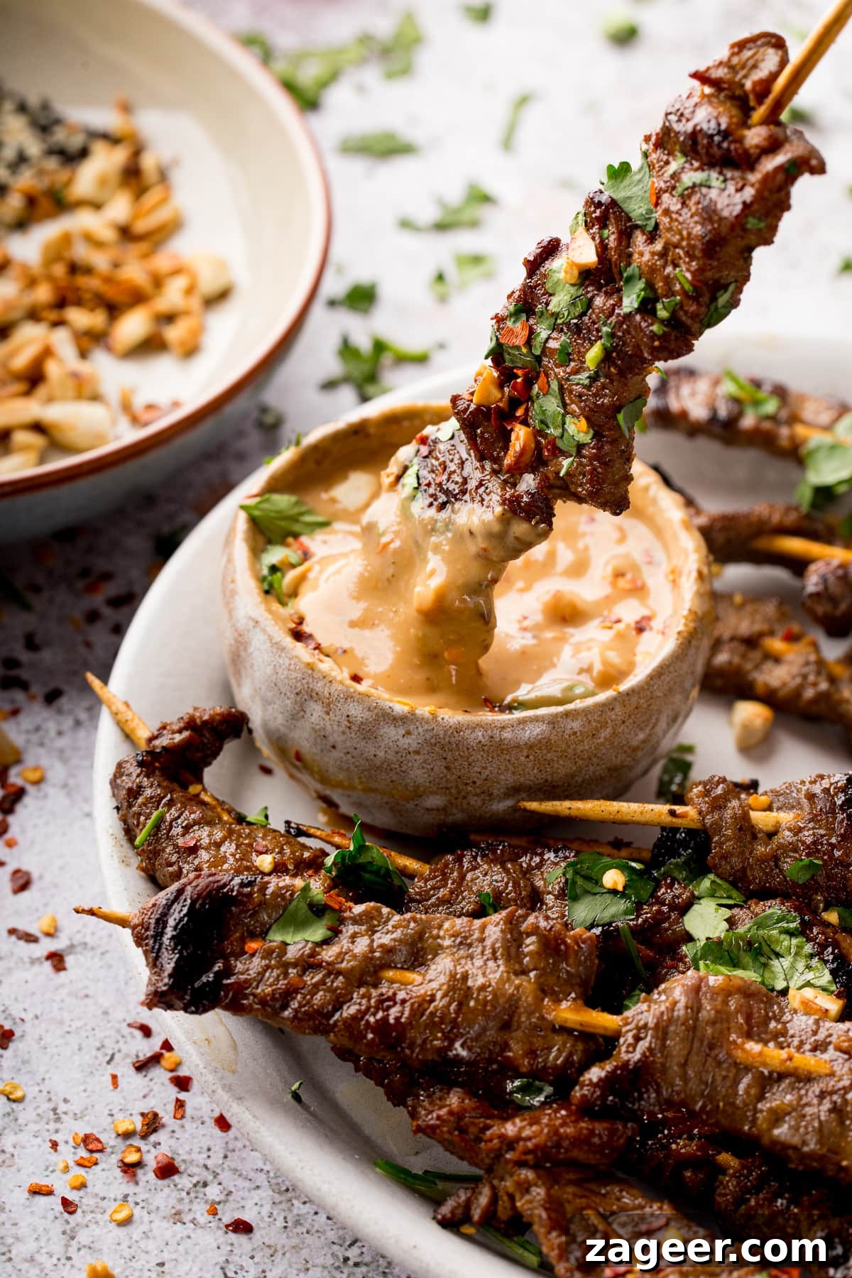 Grilled Beef Satay Recipe: Tender Skewers with Peanut Sauce 9 beef satay skewer being dipped into satay sauce.