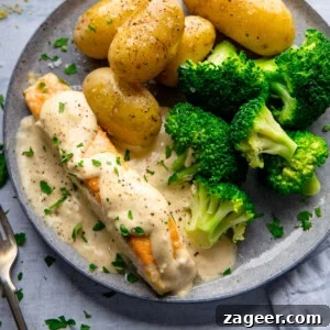 A plate with boiled potatoes, steamed broccoli, and pan fried salmon fillet topped with a creamy white sauce, garnished with chopped parsley.