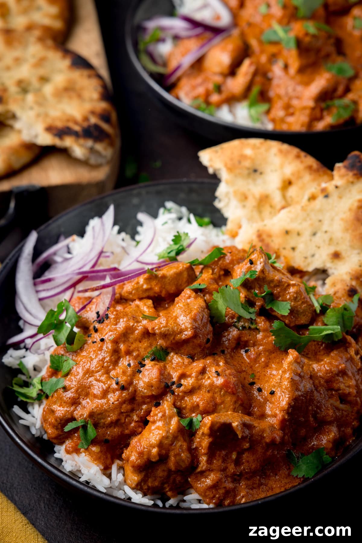 Slow-Cooker Butter Chicken Recipe for Tender, Creamy Meals 2 A bowl full of boiled rice and crock pot butter chicken with some sliced red onion and naan bread in the corner of the bowl.