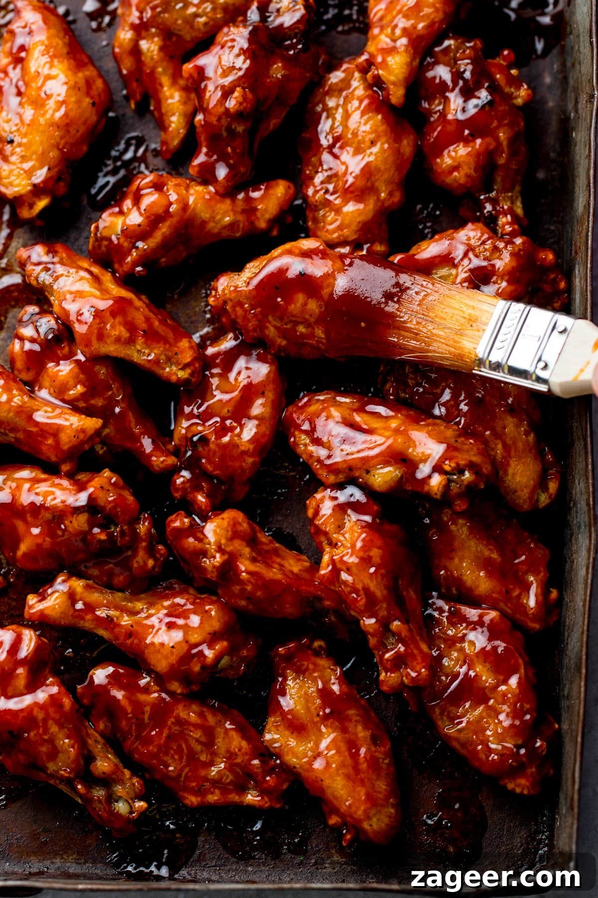 Perfect BBQ Chicken Wings Recipe: Juicy, Crispy & Smoky 2 Tall image of BBQ chicken wings on a baking tray with sauce being brushed on
