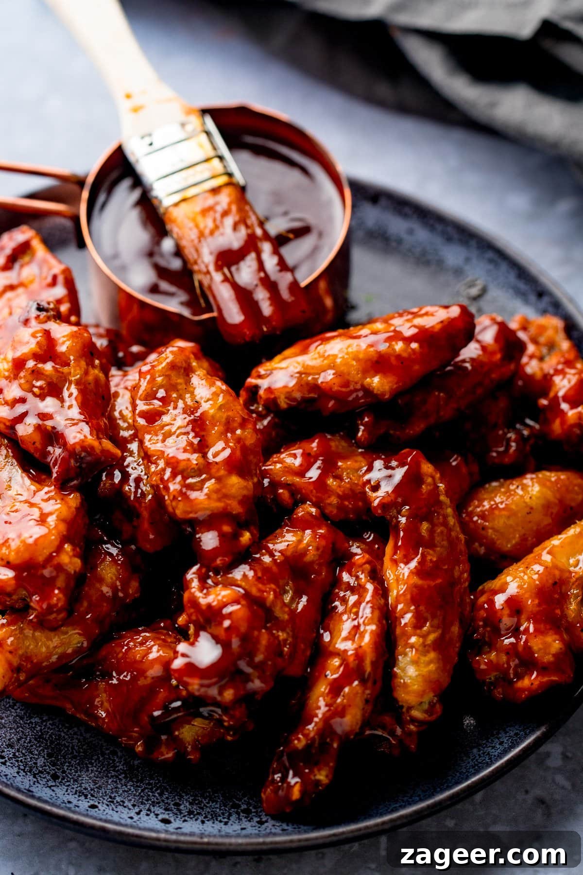 Perfect BBQ Chicken Wings Recipe: Juicy, Crispy & Smoky 9 BBQ chicken wings on a black plate with a pot of BBQ sauce and a brush on top.