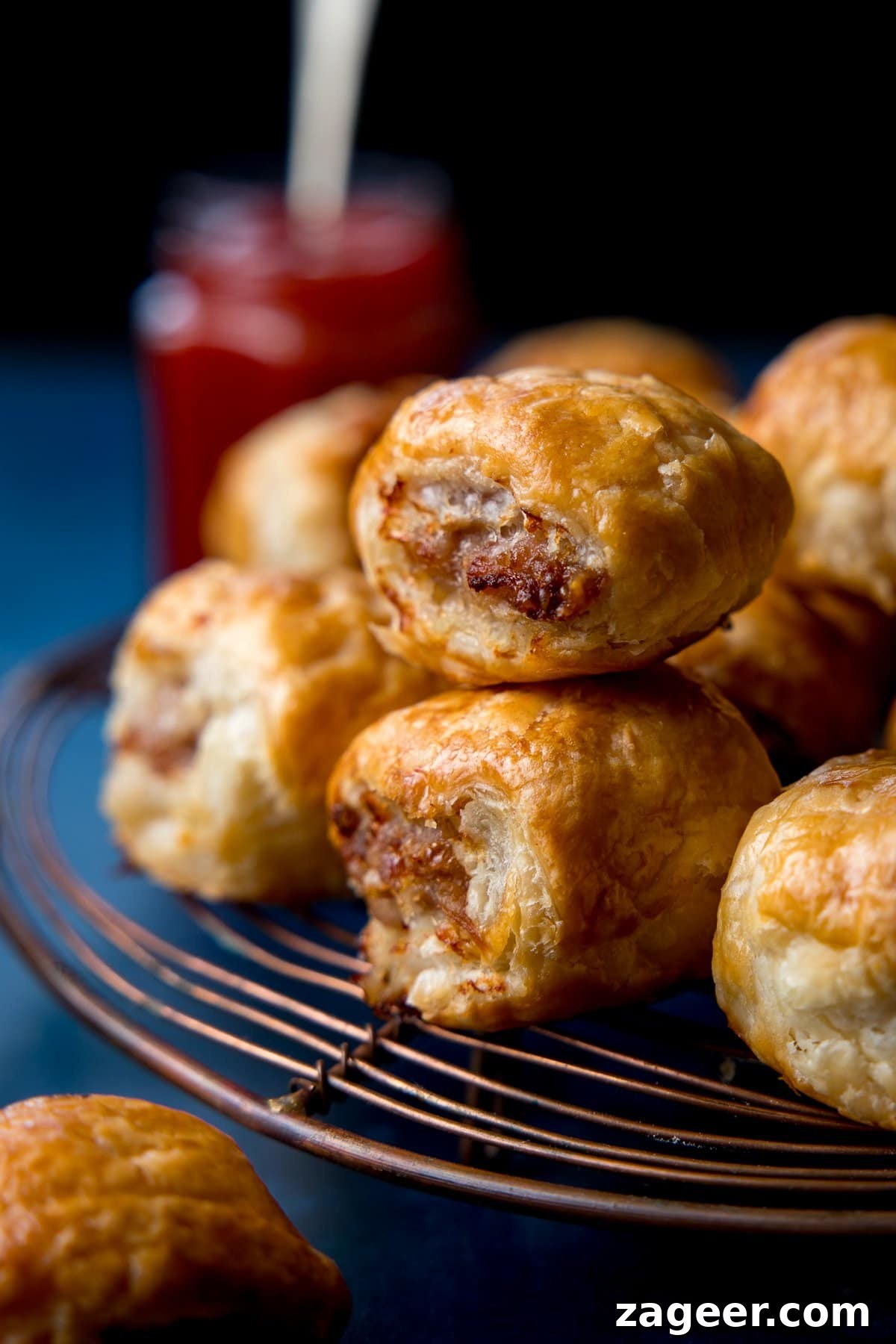 Crispy Homemade Sausage Rolls Recipe for Perfect Party Snacks 7 close up of two sausage rolls on a cooling rack. Pot of ketchup in the background