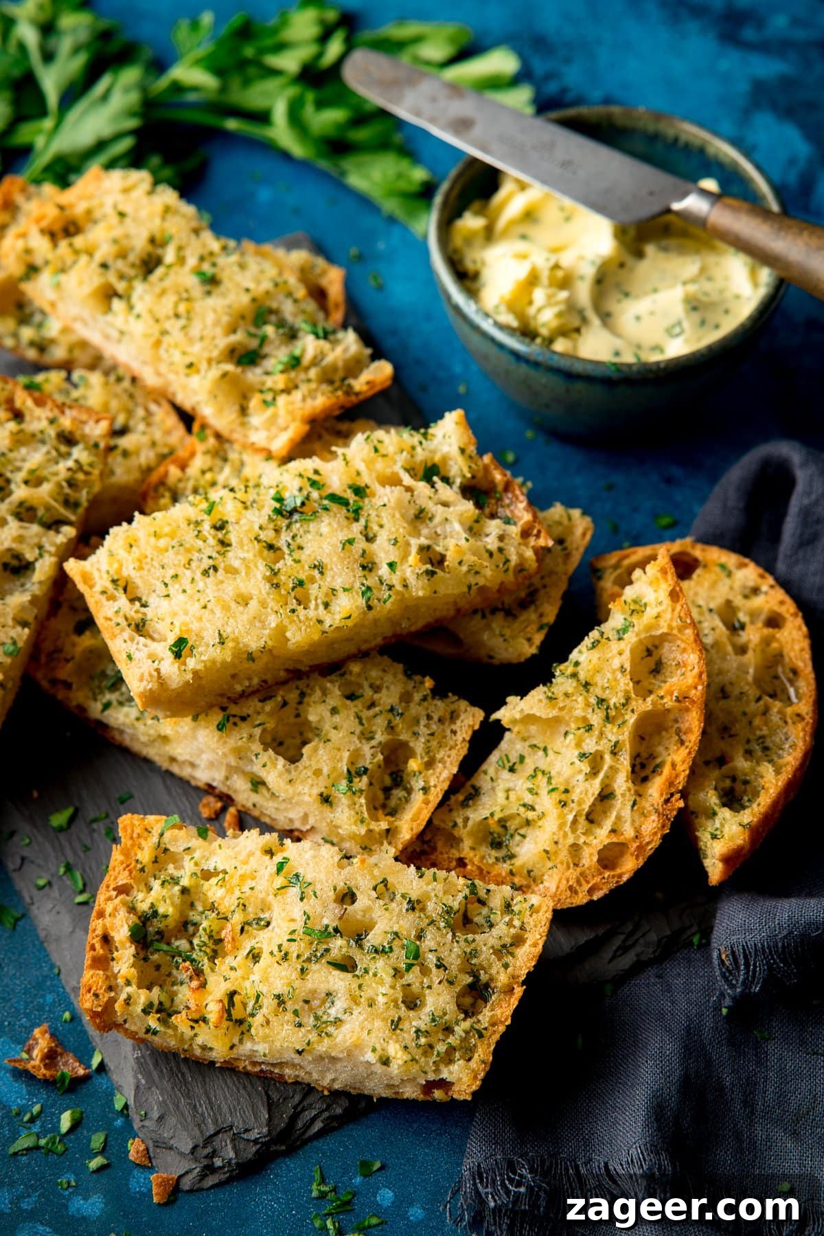 Quick Homemade Garlic Bread Recipe for Crispy, Flavorful Slices 6 Slices of garlic bread on a slate board on a dark blue background with bowl of garlic butter and knife next to it
