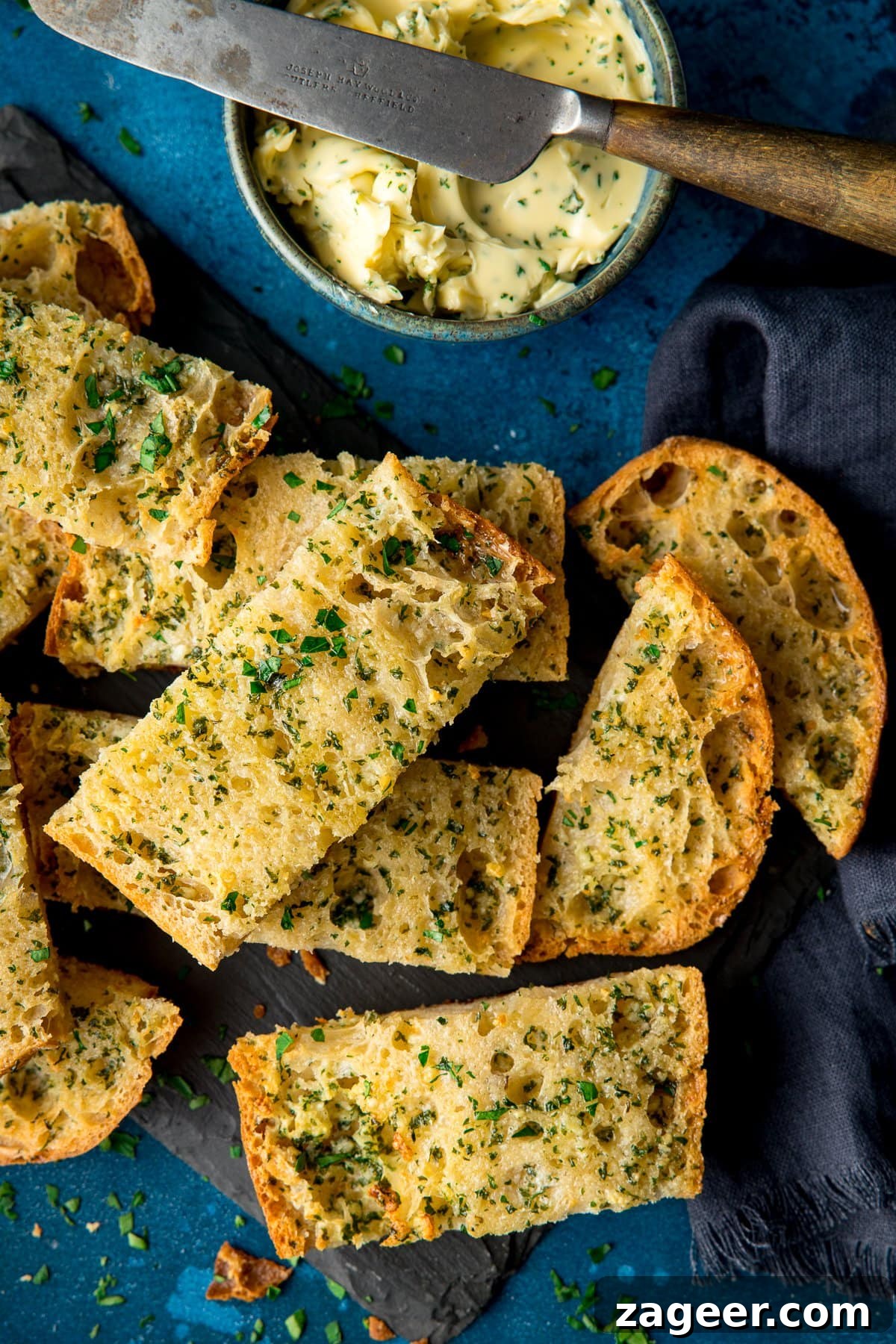 Quick Homemade Garlic Bread Recipe for Crispy, Flavorful Slices 7 Overhead of slices of garlic bread on a dark background with bowl of garlic butter at top of the frame