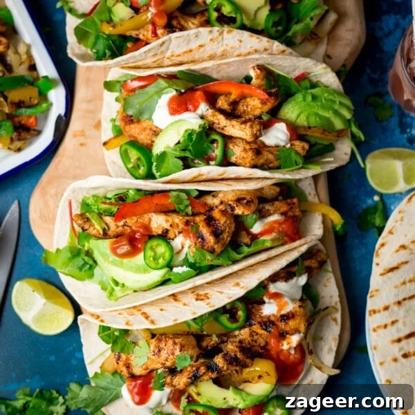 Authentic Lamb Barbacoa Recipe — Slow-Cooked Mexican-Style Lamb 8 Three grilled chicken tacos with avocado, soured cream, jalapeños, coriander, and salsa on flour tortillas, served with lime wedges on a blue surface.