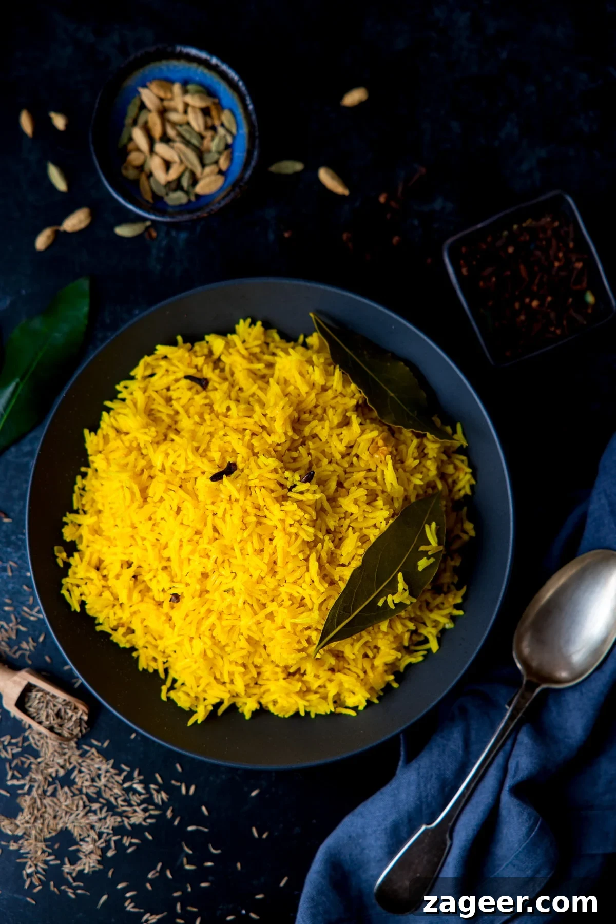 Authentic Pilau Rice Recipe: Aromatic Spiced Pilaf Instructions 2 Pilau rice in a black bowl on a dark surface with ingredients scattered around