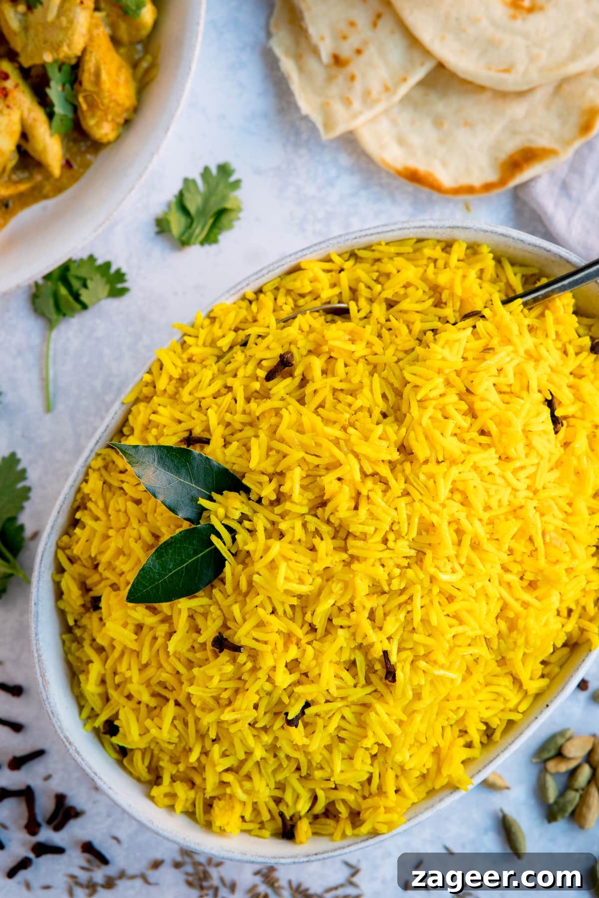 Authentic Pilau Rice Recipe: Aromatic Spiced Pilaf Instructions 6 Pilau rice in a white bowl on a light background. Flatbreads and plate of curry just in frame