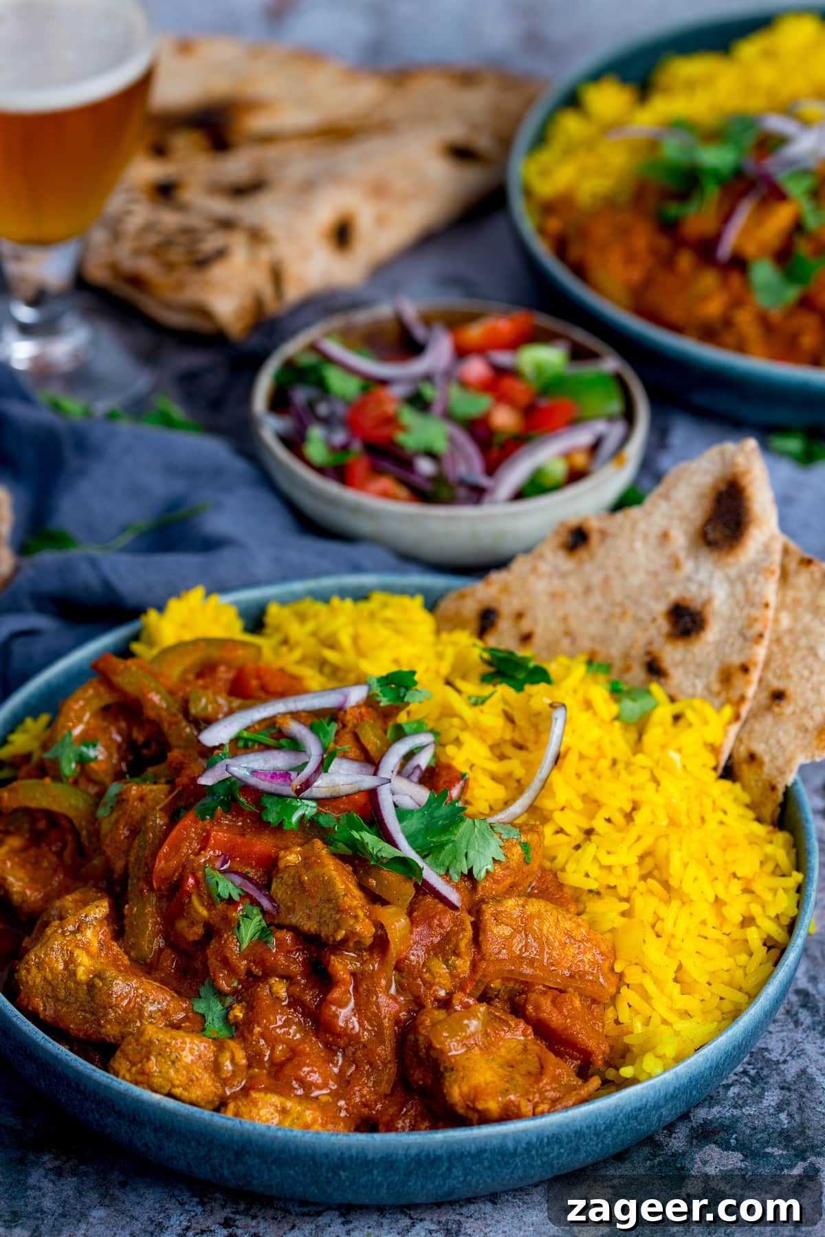 Authentic Pilau Rice Recipe: Aromatic Spiced Pilaf Instructions 7 Pilau rice with chicken jalfrezi in a blue bowl on a blue background. Further dishes scattered around.
