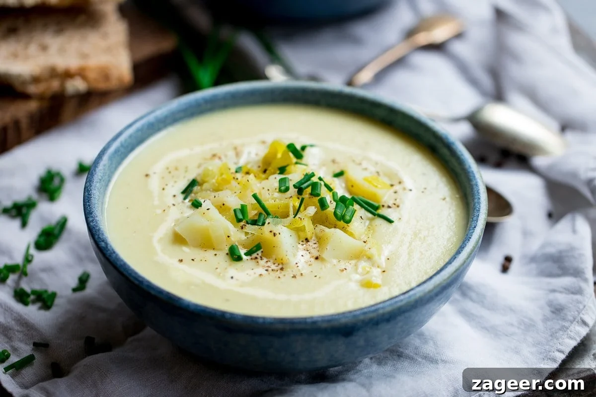 Creamy Leek and Potato Soup Recipe with Fresh Herbs 5 Wide image of a blue bowl filled with leek and potato soup, topped with potatoes and chives.