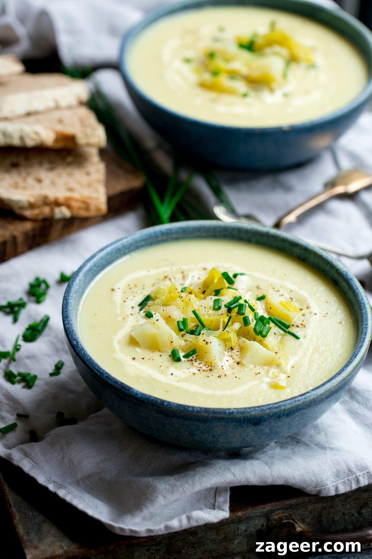 Creamy Leek and Potato Soup Recipe with Fresh Herbs 6 Blue bowl filled with leek and potato soup, topped with potato and chives. Second bowl in the background.