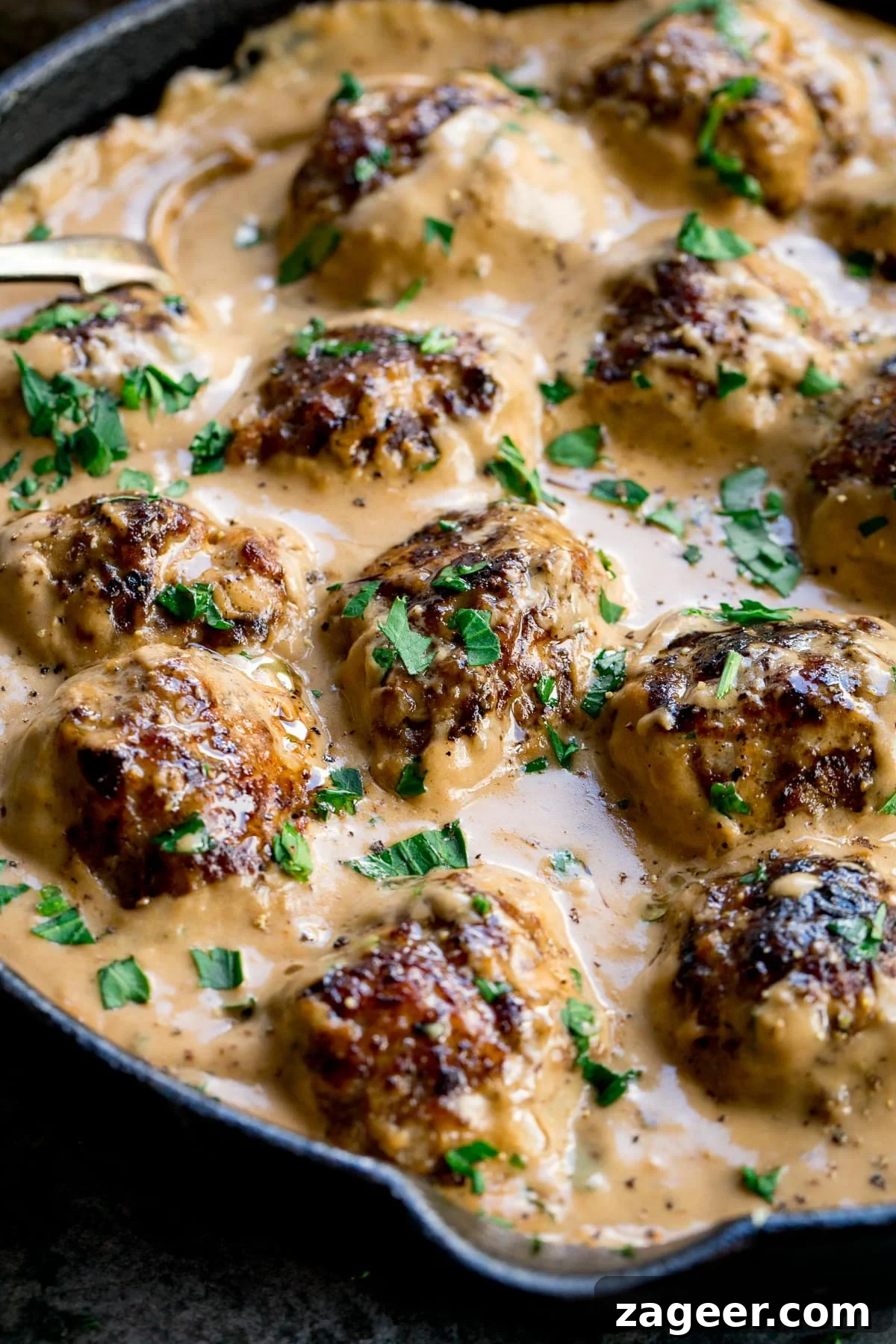 Authentic Swedish Meatball Recipe with Creamy Gravy and Lingonberry 2 Close up of Swedish meatballs and gravy in a pan topped with parsley