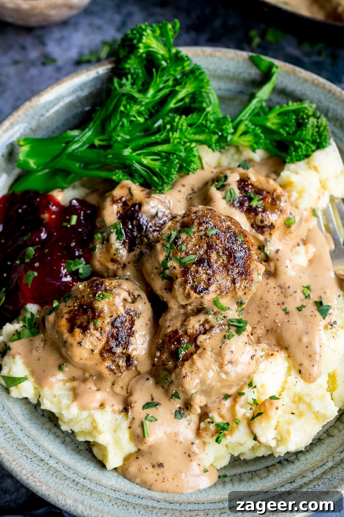 Authentic Swedish Meatball Recipe with Creamy Gravy and Lingonberry 9 Swedish meatballs on top of mashed potatoes in a bowl with lingonberry jam and broccoli