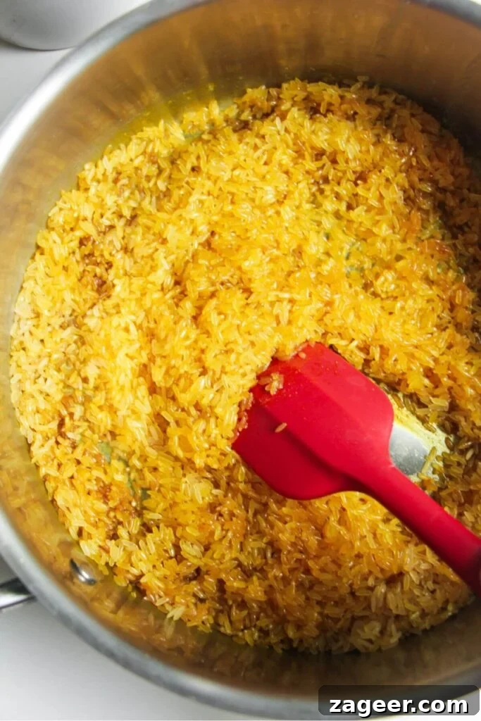 Mediterranean Ground Beef and Rice Bowls with Feta & Herbs 6 Red spatula stirring rice through spices in a large pot.