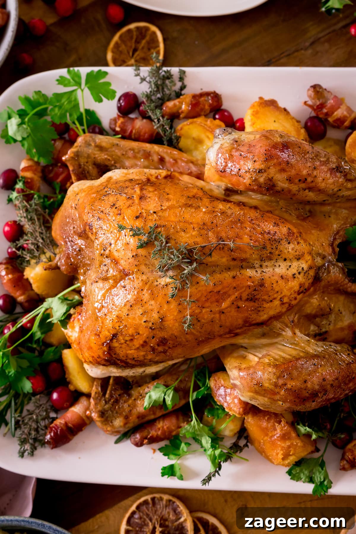 Roast turkey on a white plate surrounded by fresh herbs, cranberries and other garnishes.