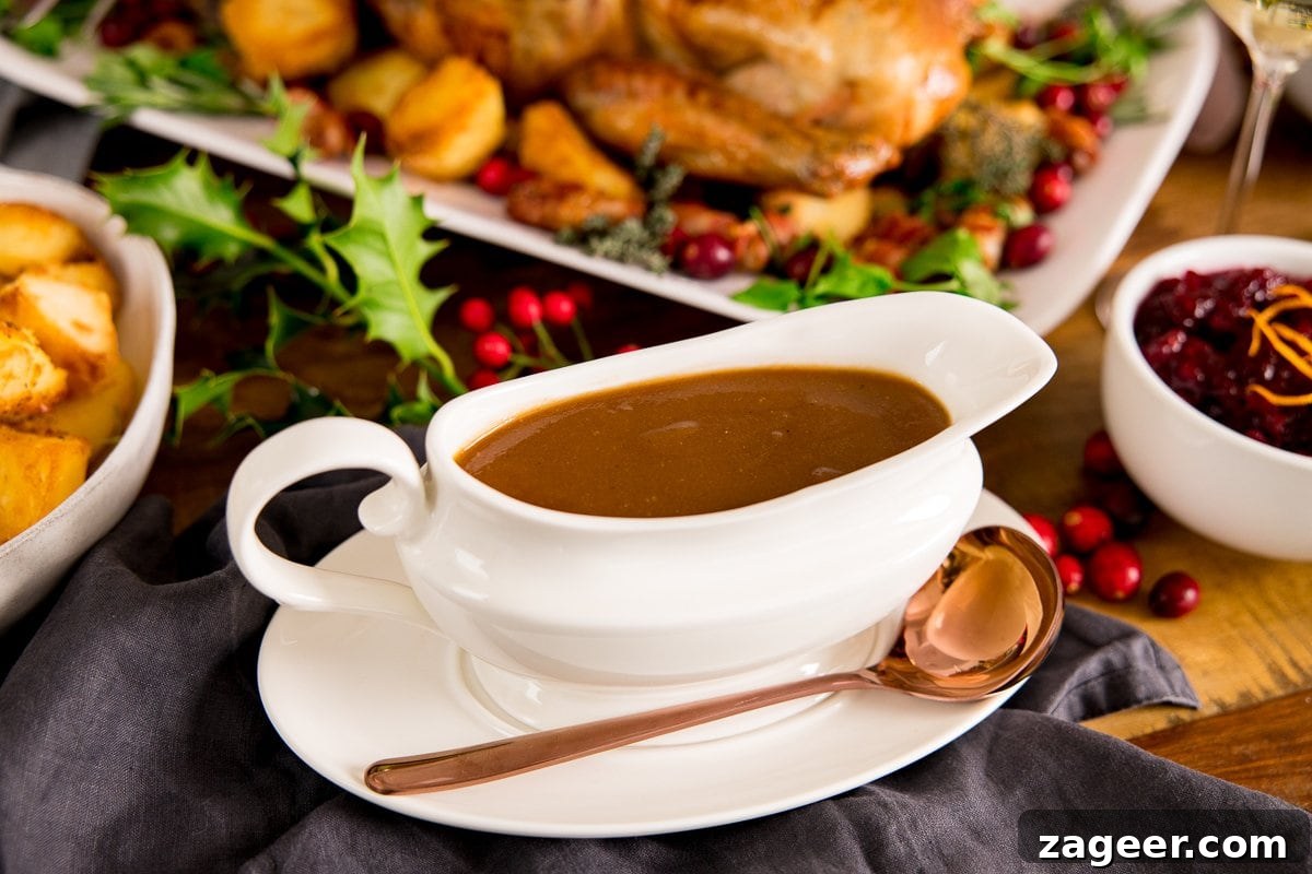 A white gravy boat filled with gravy on a table with a roast turkey and side dishes around the gravy boat.