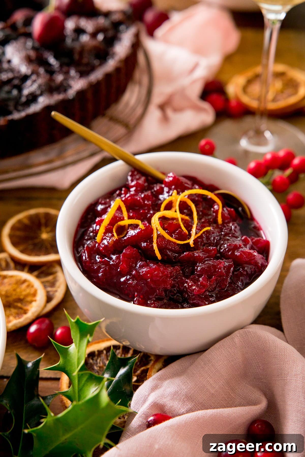 Port-Infused Cranberry Sauce Recipe for Holiday Menus 2 Cranberry sauce in a white bowl, topped with orange zest. Festive table decorations scattered around the bowl.